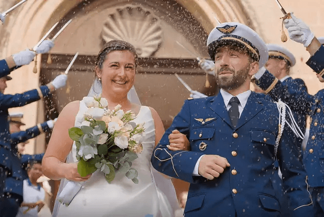 Une mariée souriante, un bouquet à la main, sort d'une église au bras de son époux en uniforme, sous une haie d'honneur de militaires sabres levés et une pluie de riz